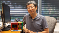 A man poseses with a table sized 3D printed model of the Solenoidal Large Intensity Device.