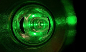 A close-up view of a green laser beam inside a reflective cylindrical chamber, which is the Compton polarimeter’s laser system